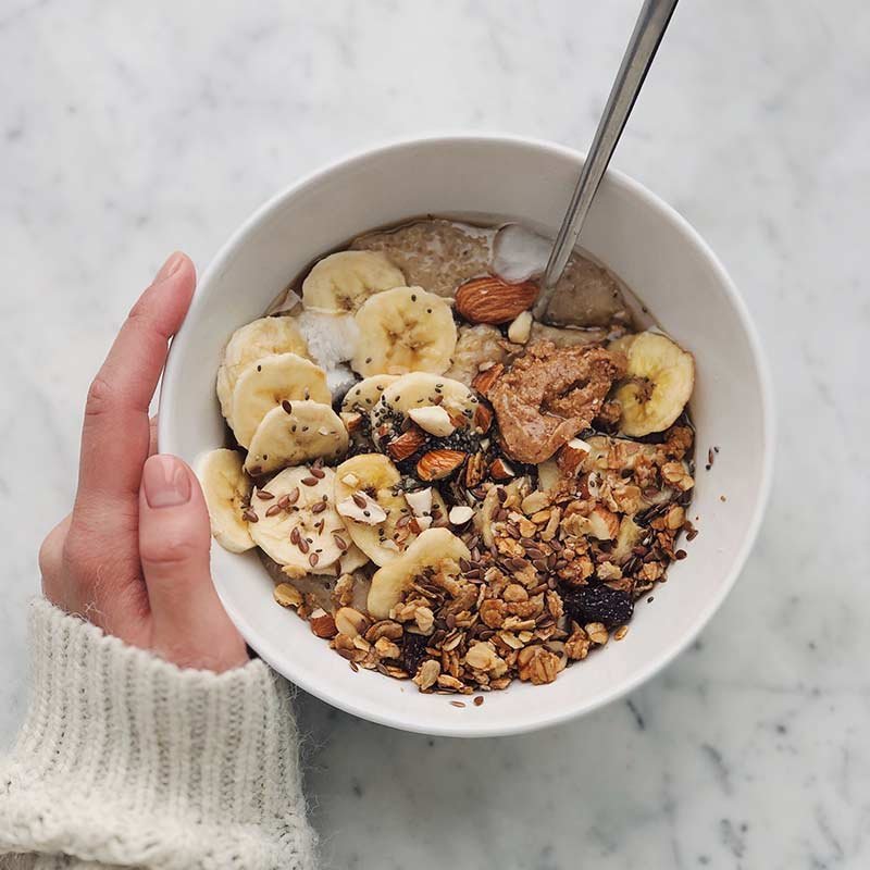 a hand holding a bowl of oatmeal with granola, bananas, and nuts